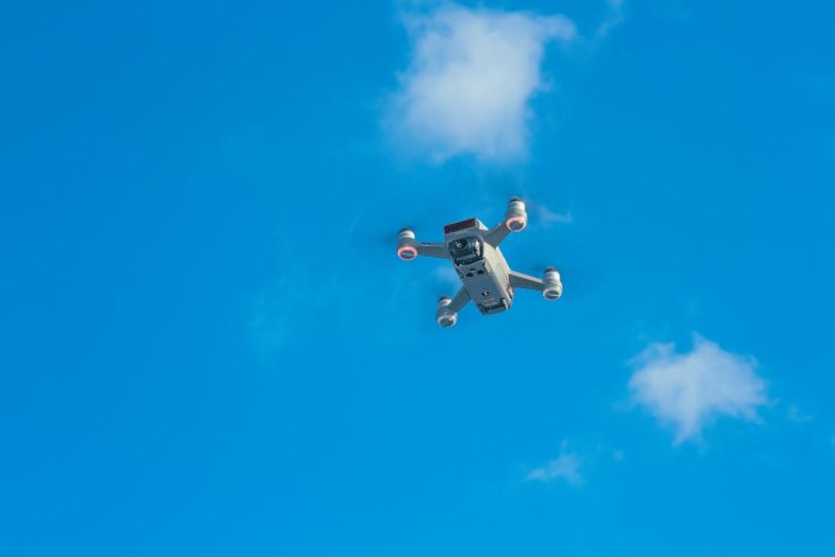 Aerial view of a drone cruising in a bright blue sky with scattered clouds.